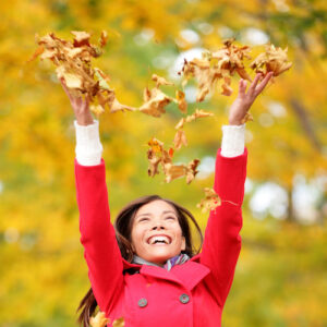 Happy fall xwoman throwing autumn leaves up in the air smiling blissful and cheerful in autumn forest. Young beautiful multicultural Caucasian / Asian xwoman model outside.